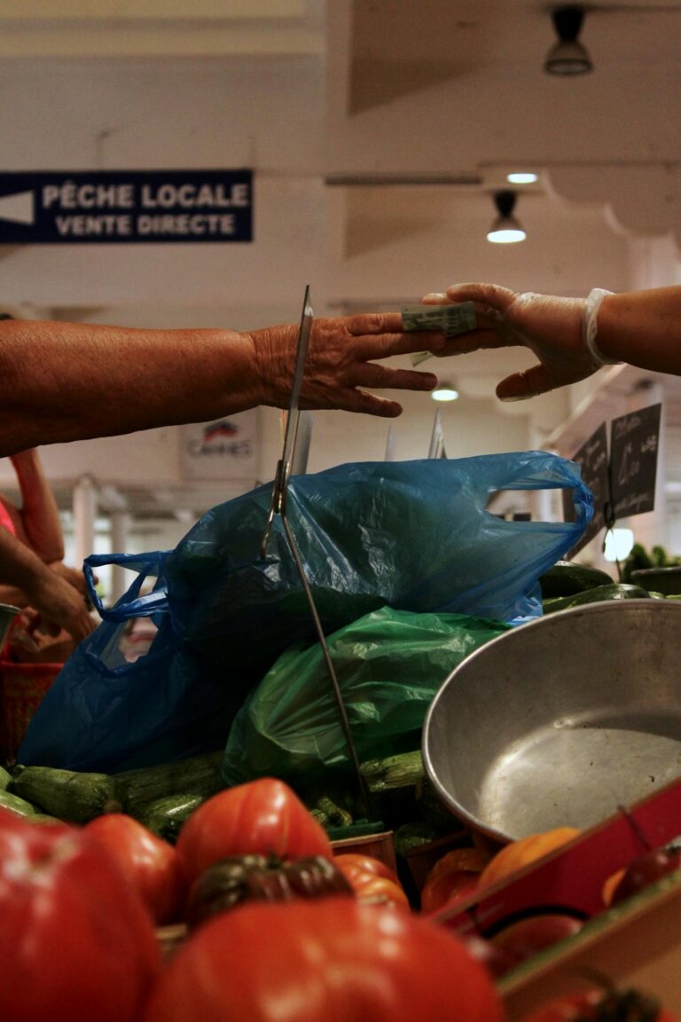 Hands exchanging cash at a local market vendor, with fresh vegetables in focus.